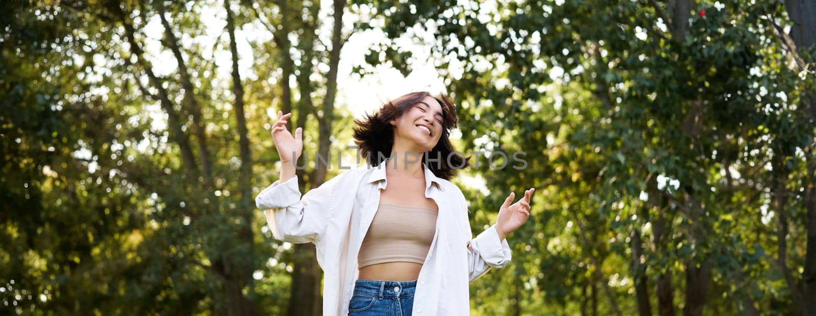 Happy people. Carefree asian girl dancing and enjoying the walk in park, feeling happiness and joy, triumphing.