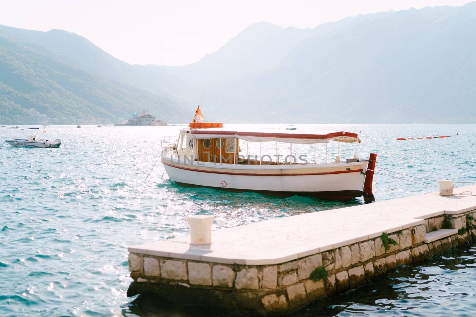 Excursion boat is moored to the bollard on the pier in the sea against the backdrop of the mountains by Nadtochiy