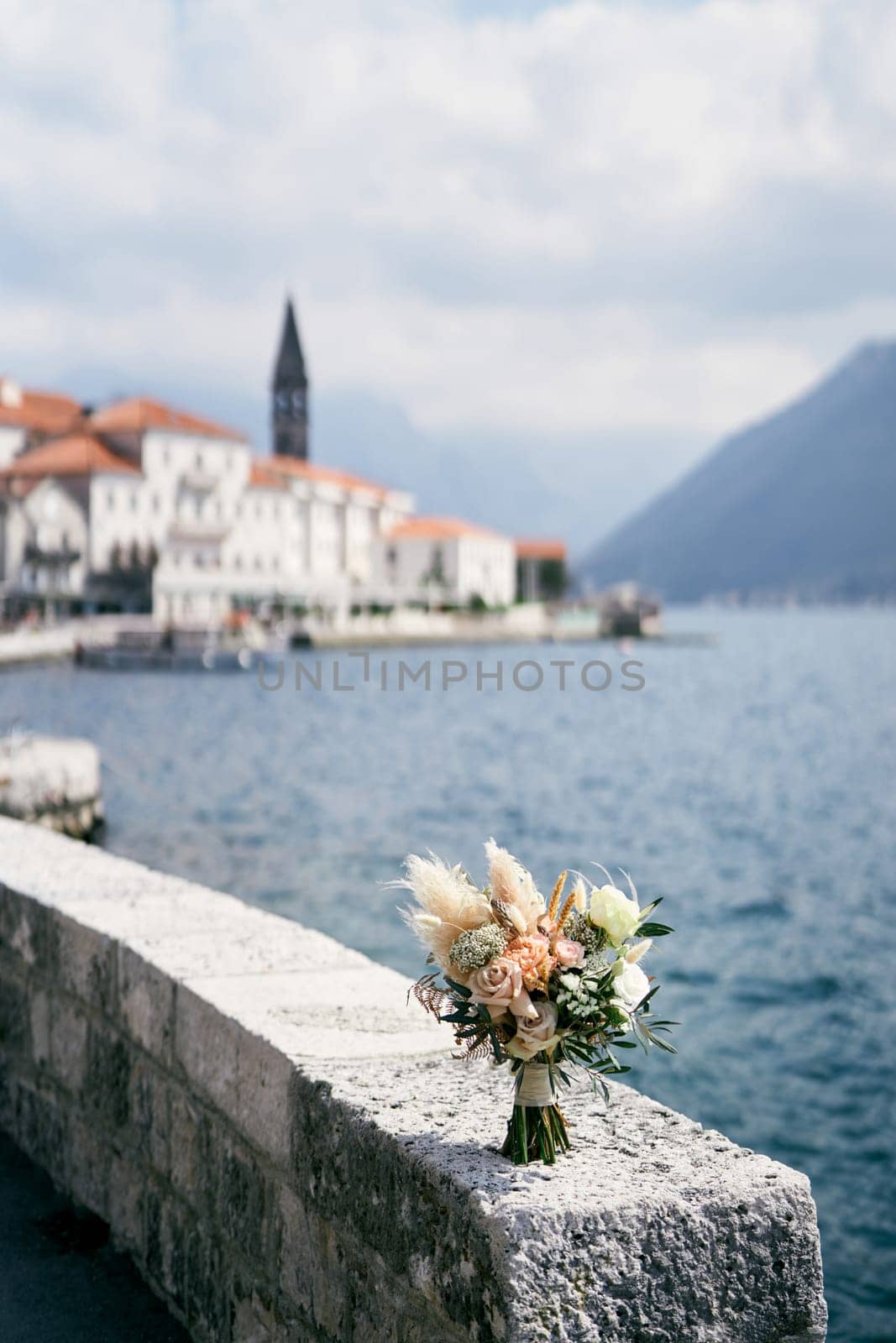 Bridal bouquet stands on a stone fence over the sea on the shore of an old town. High quality photo