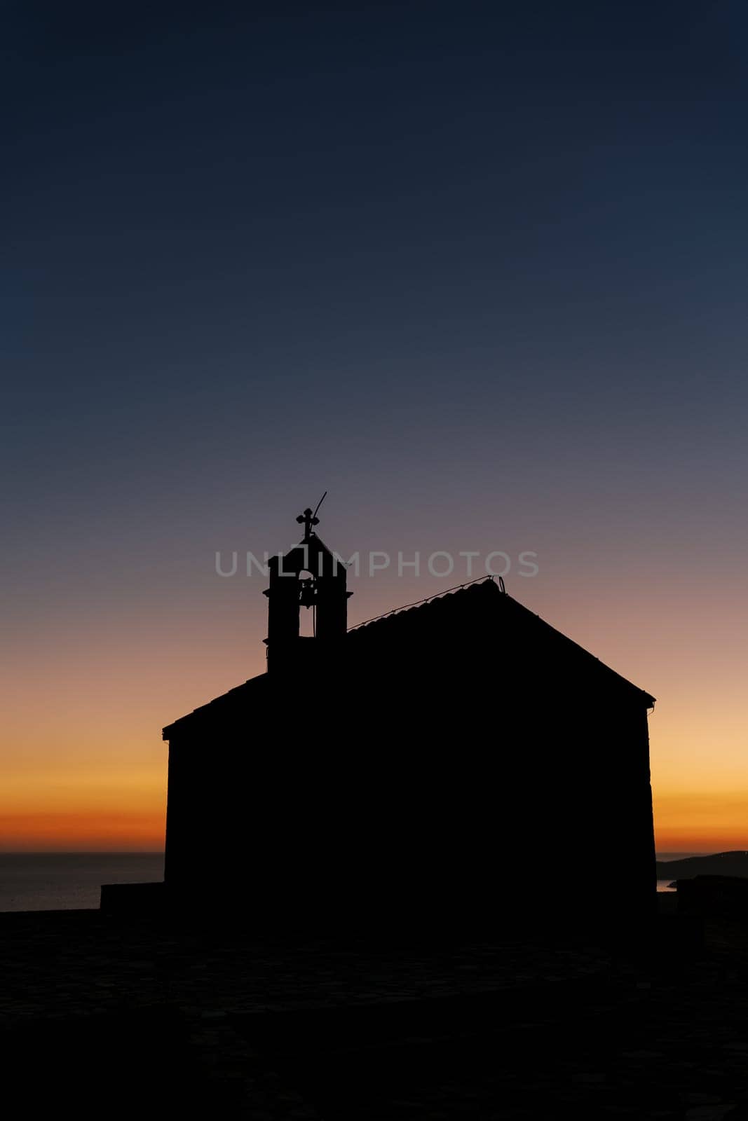 Silhouette of a church with a bell tower on the roof against the sunset sky by Nadtochiy