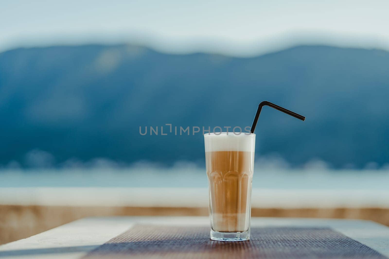 Glass with a latte with a straw stands on a cafe table. High quality photo