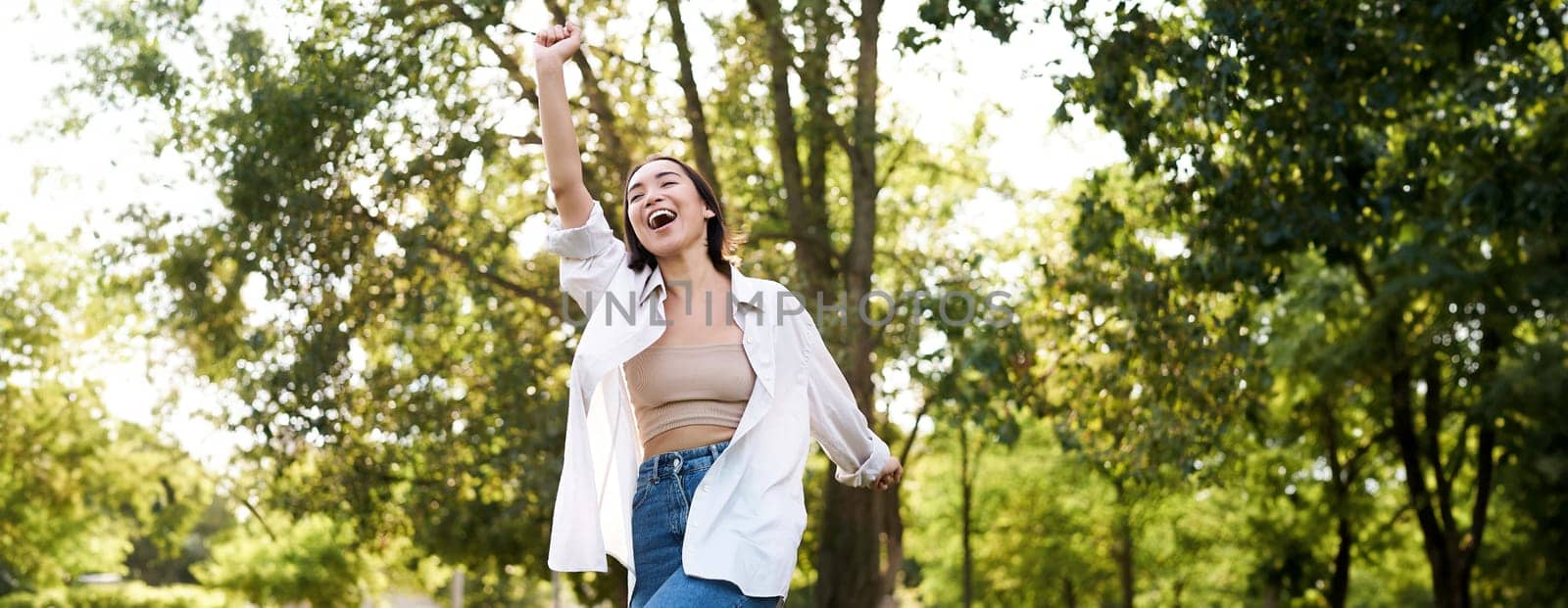 Happy people. Carefree asian girl dancing and enjoying the walk in park, feeling happiness and joy, triumphing.