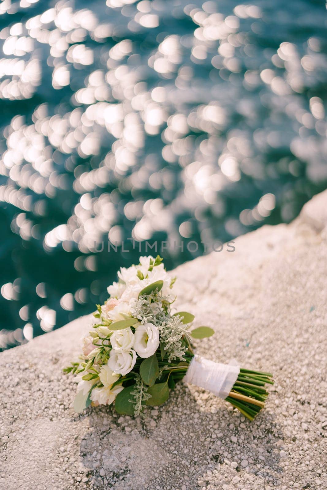 Bridal bouquet lies on a stone border near the shining water by Nadtochiy