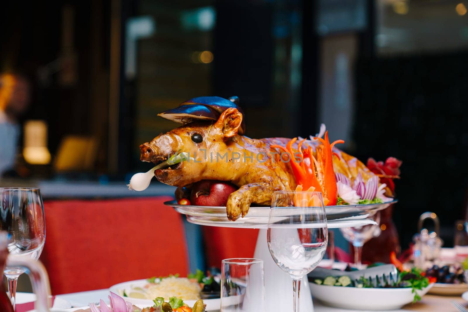 Roasted pig garnished with vegetables lies on a dish on a table in a restaurant. High quality photo
