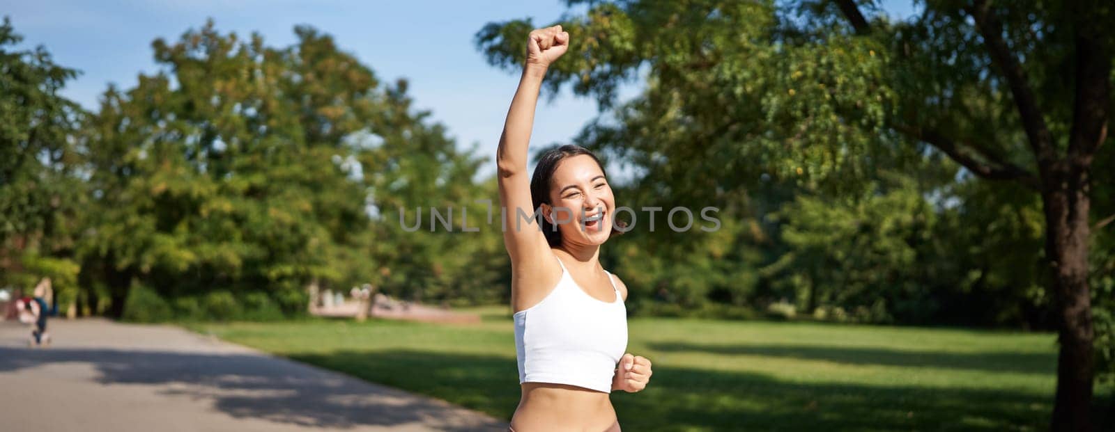Hooray, victory. Smiling asian girl triumphing, celebrating achievement, running till finish, shouting from excitement.