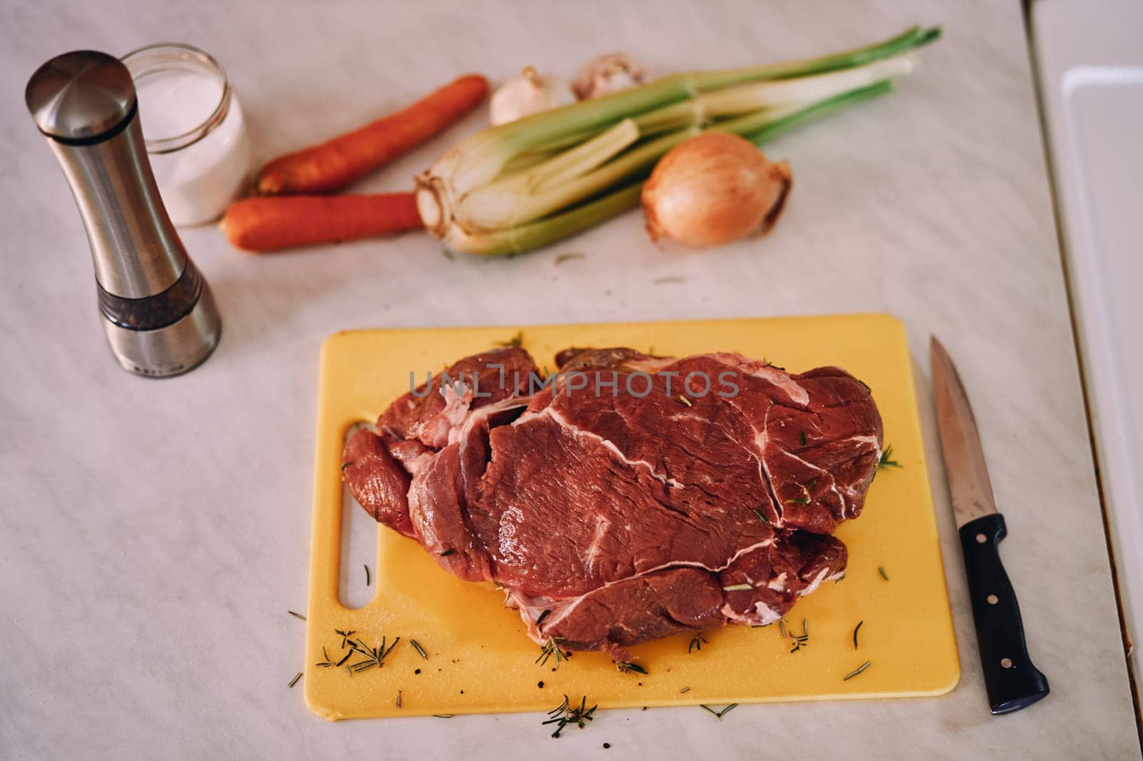 Piece of tenderloin sprinkled with rosemary lies on a cutting board on a table next to raw vegetables. High quality photo
