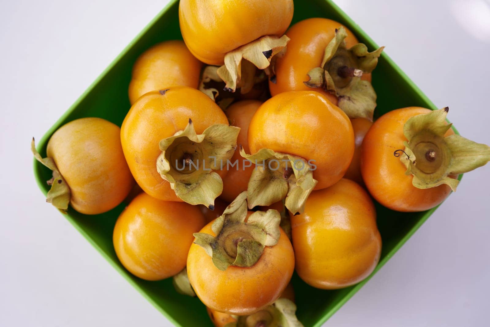 Full rhombic bowl of orange persimmons on a white table. Top view. High quality photo