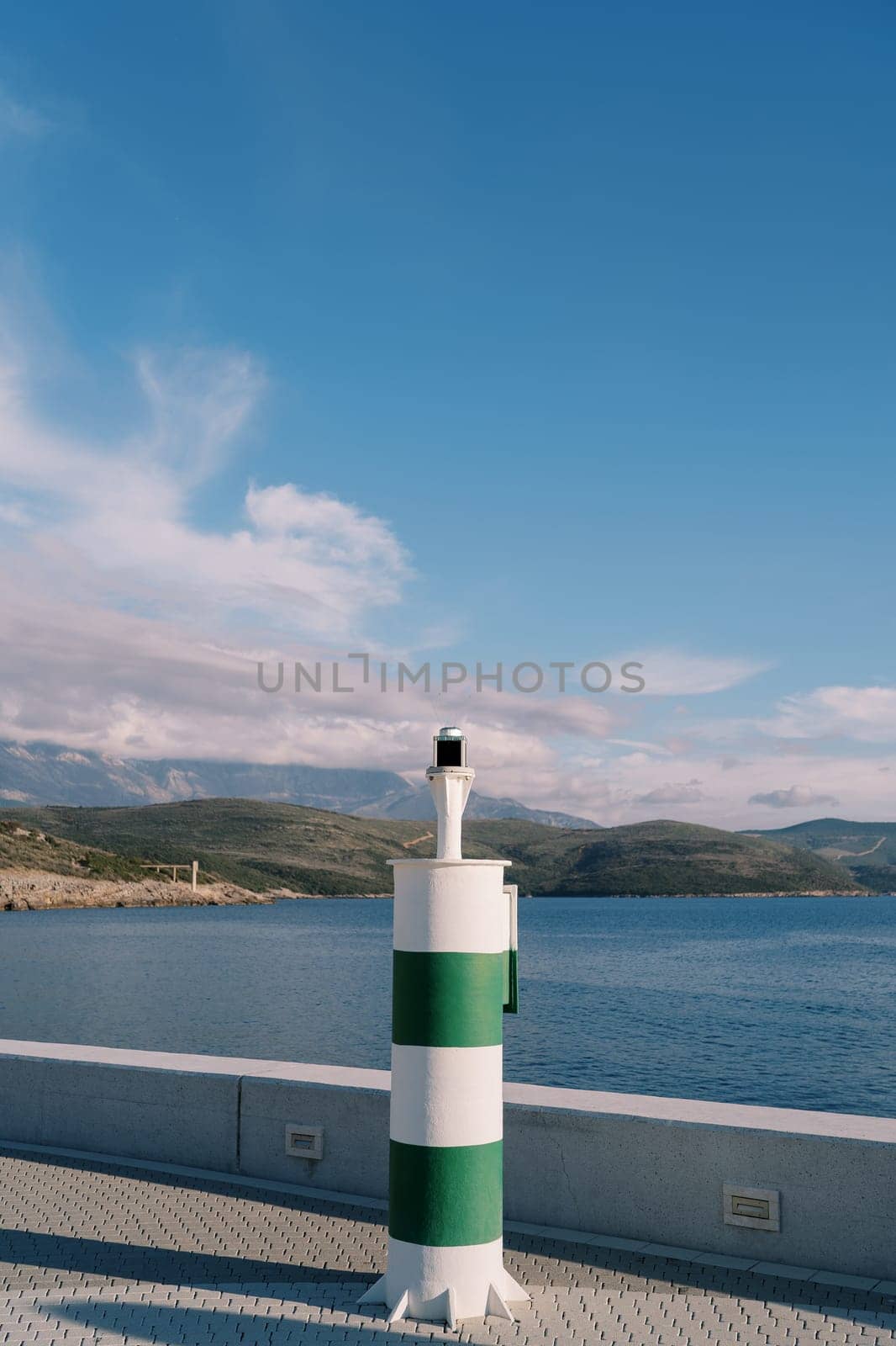 Navigation beacon on the pier against the backdrop of mountains by Nadtochiy