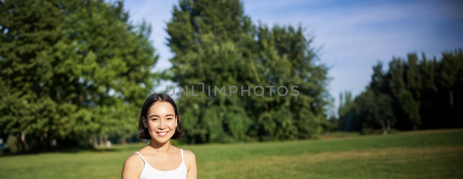 Portrait of korean girl meditating in park, follow yoga video lesson on smartphone app, sitting on fresh air and relaxing.