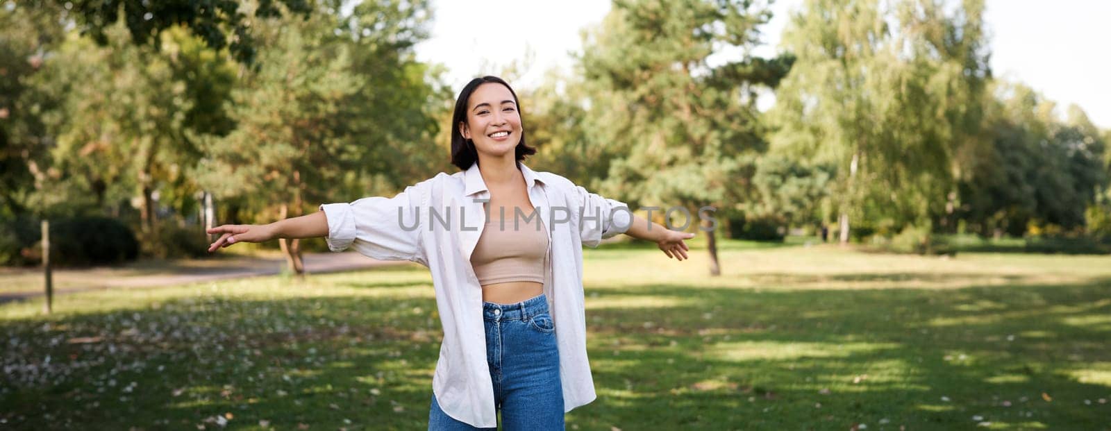 Happy asian girl dancing in park, feeling freedom and joy, walking outdoors on sunny day.