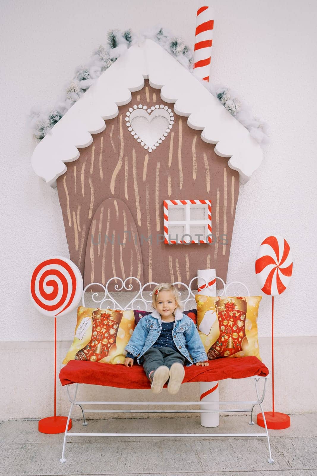 Little girl sits on a sofa in the middle of a Christmas composition by Nadtochiy