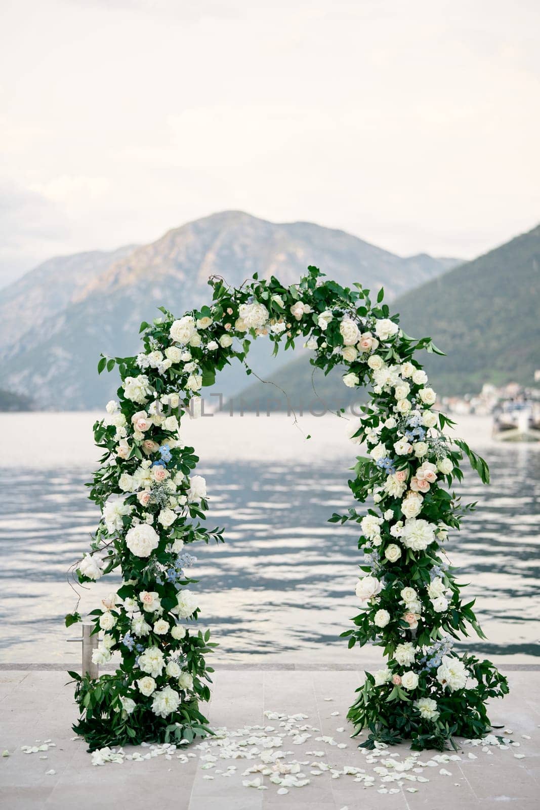 Wedding arch stands on a pier strewn with flower petals by Nadtochiy