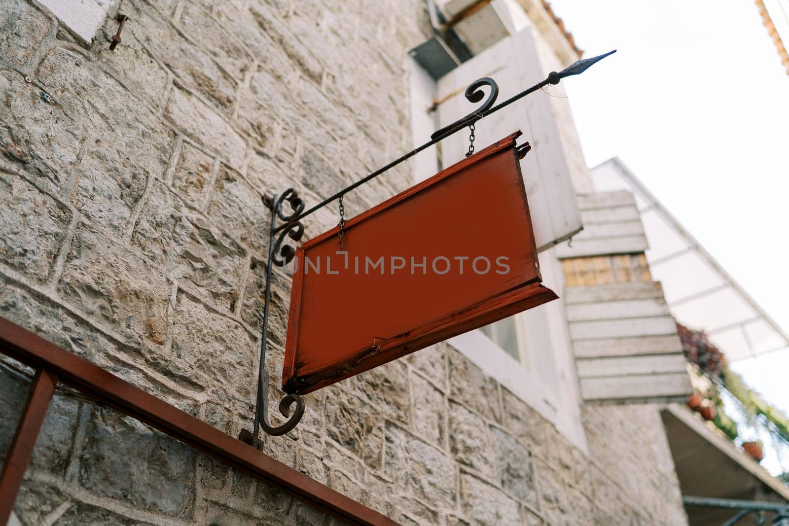 Empty tablet hangs on a forged signpost on the stone facade of an old house by Nadtochiy