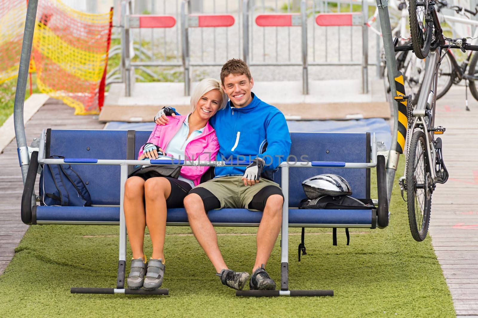 Cuddling happy couple sitting on chair lift with bicycles