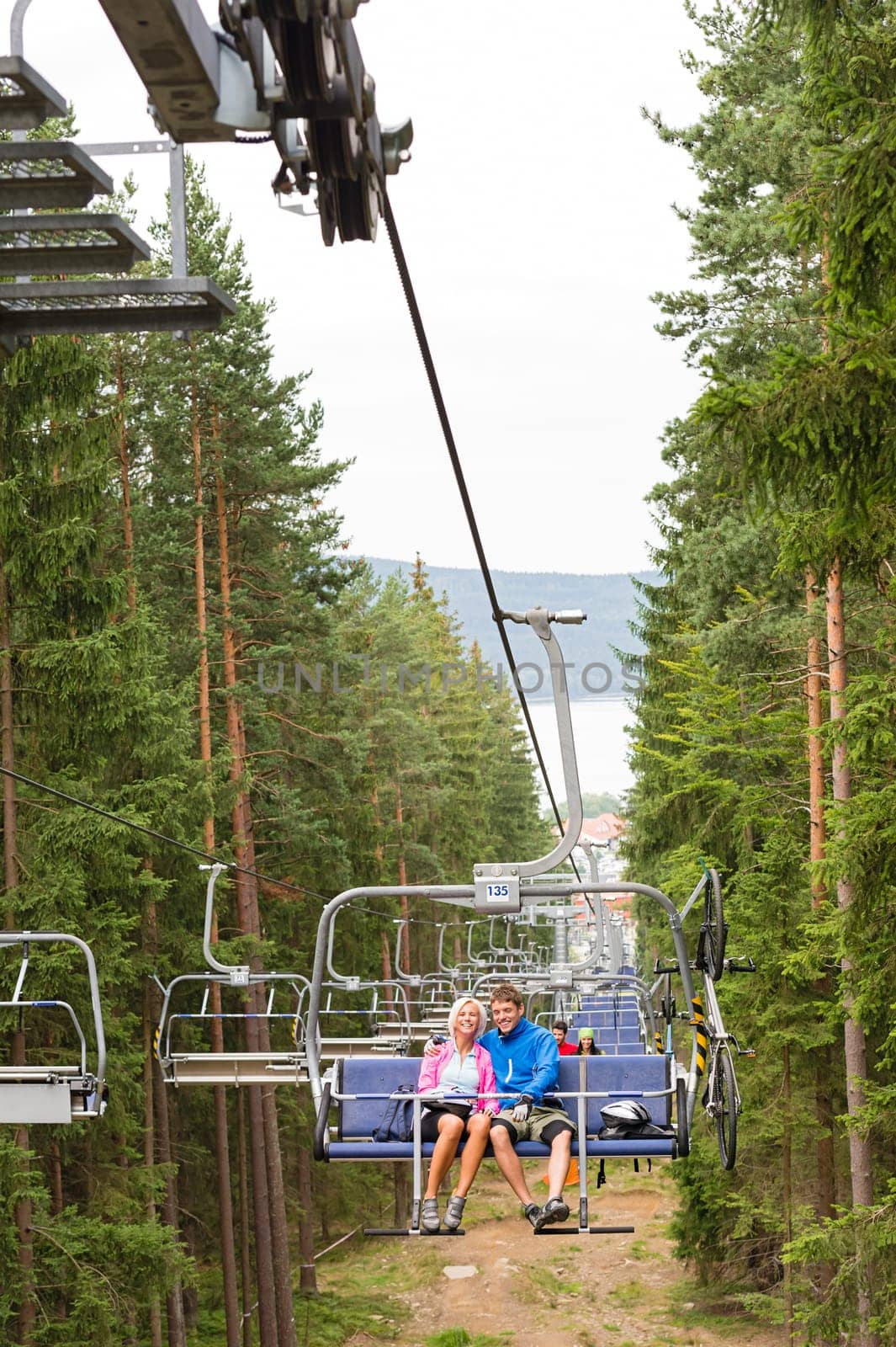 Young couple sitting on chair lift traveling through forest
