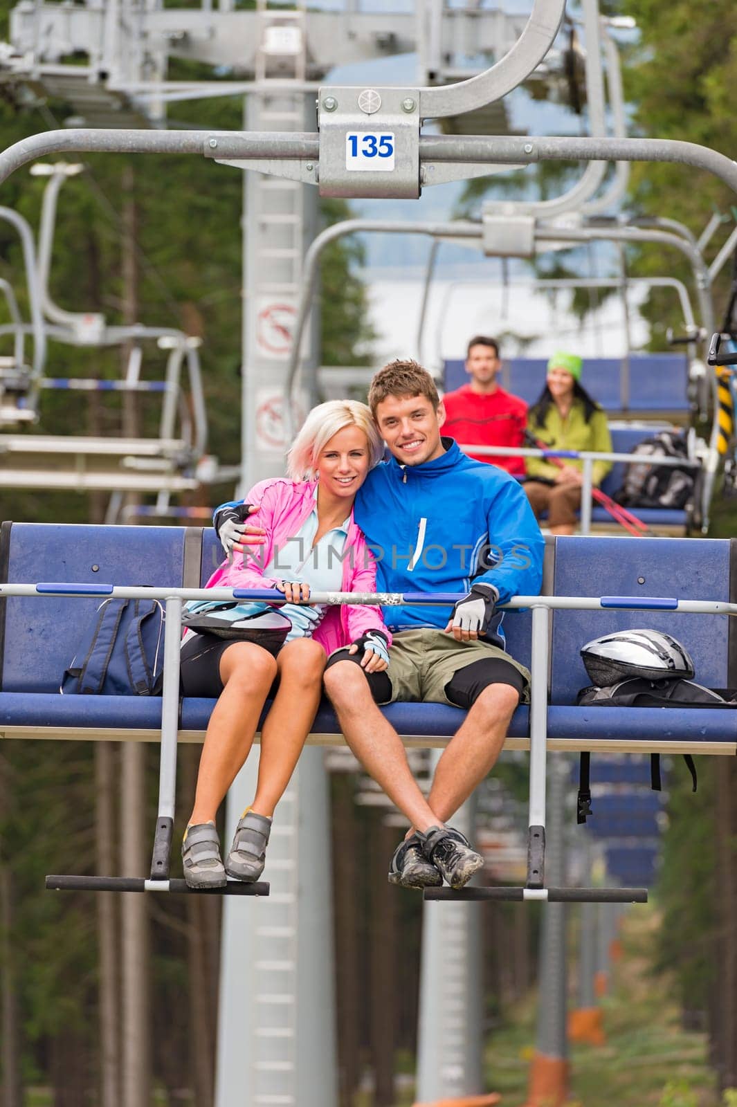 Cuddling young couple sitting on chair lift in the pinewood