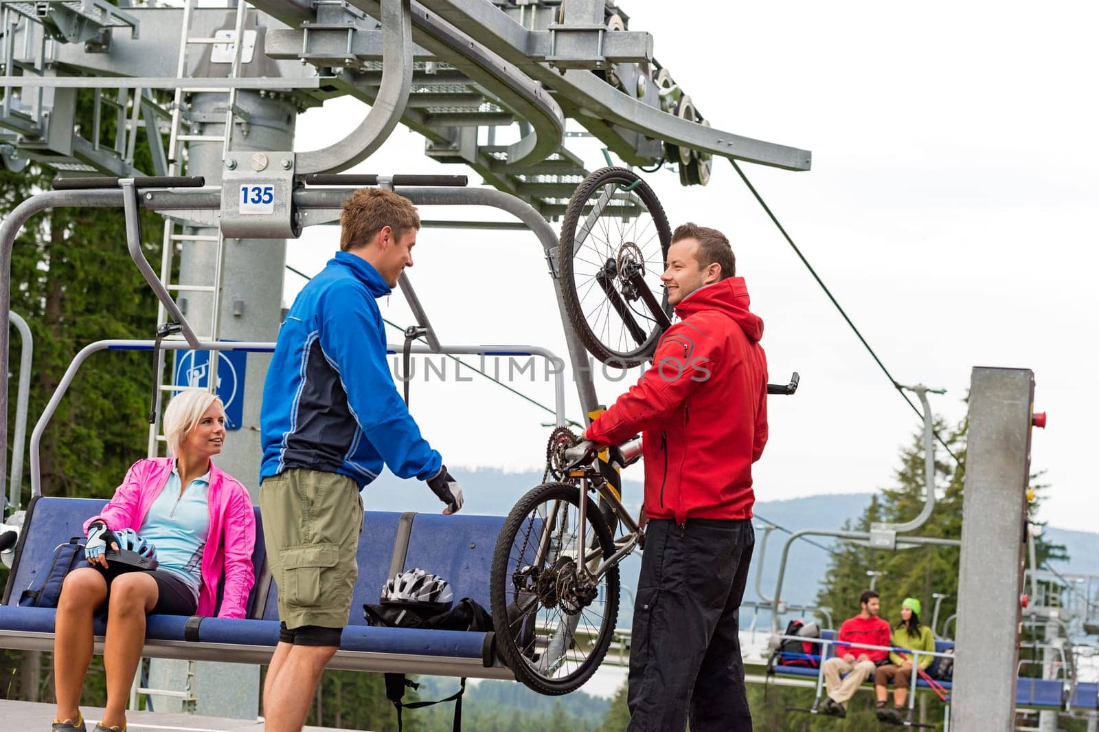 Man helping young couple taking down bicycle from chair lift