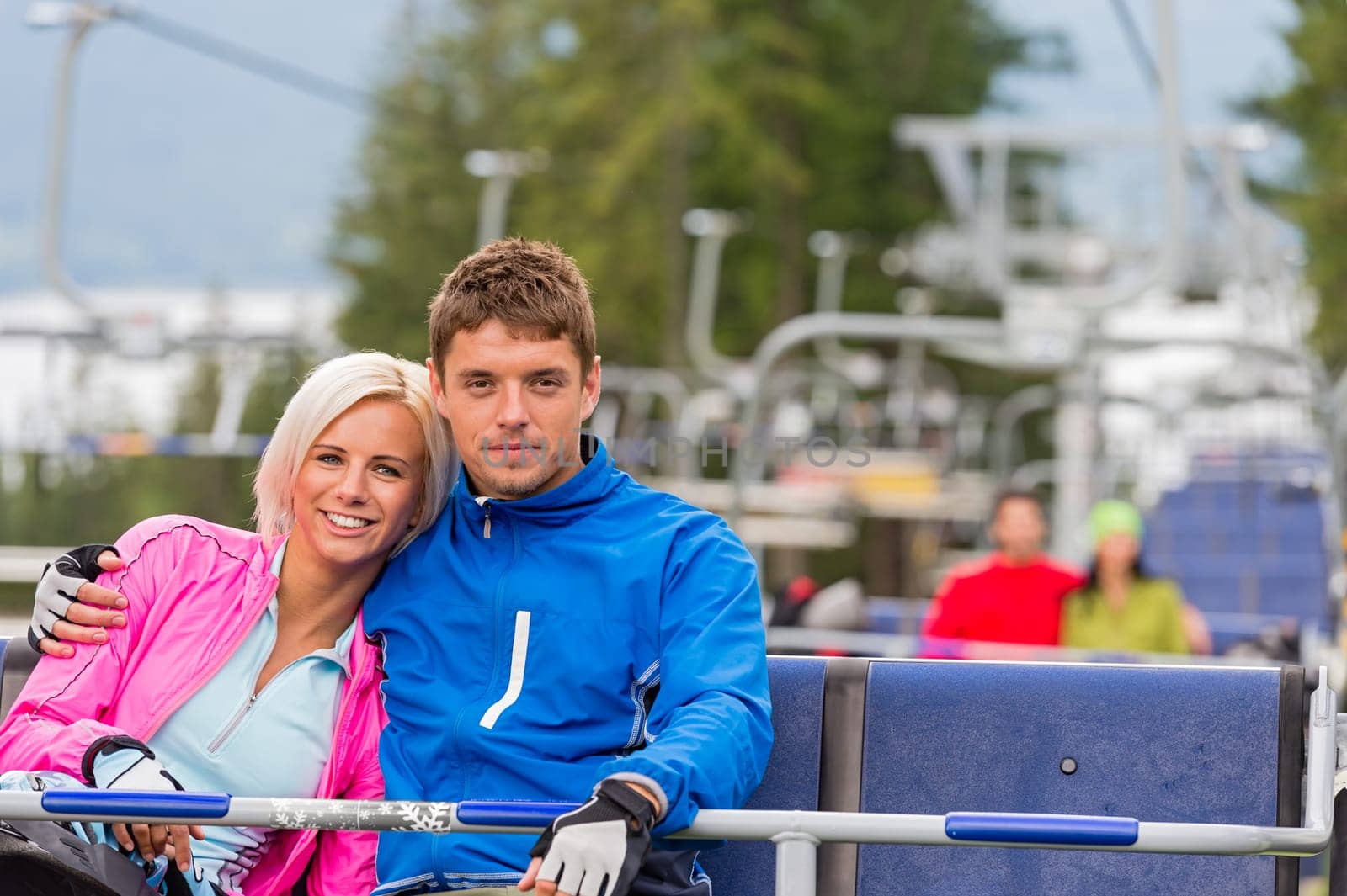 Hugging young couple in sweatsuits sitting on chair lift