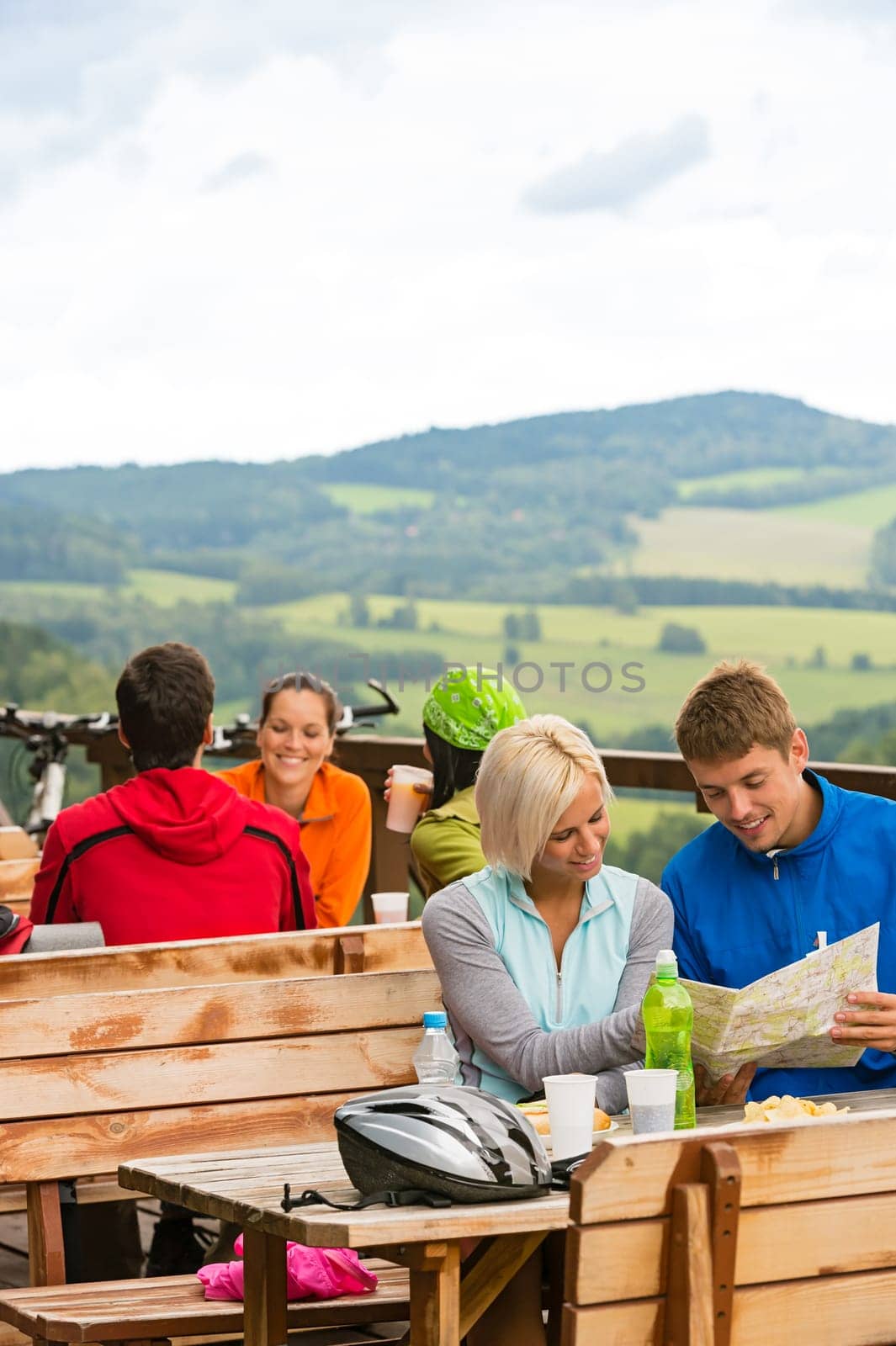 Smiling young couple resting looking at map sitting mountain countryside