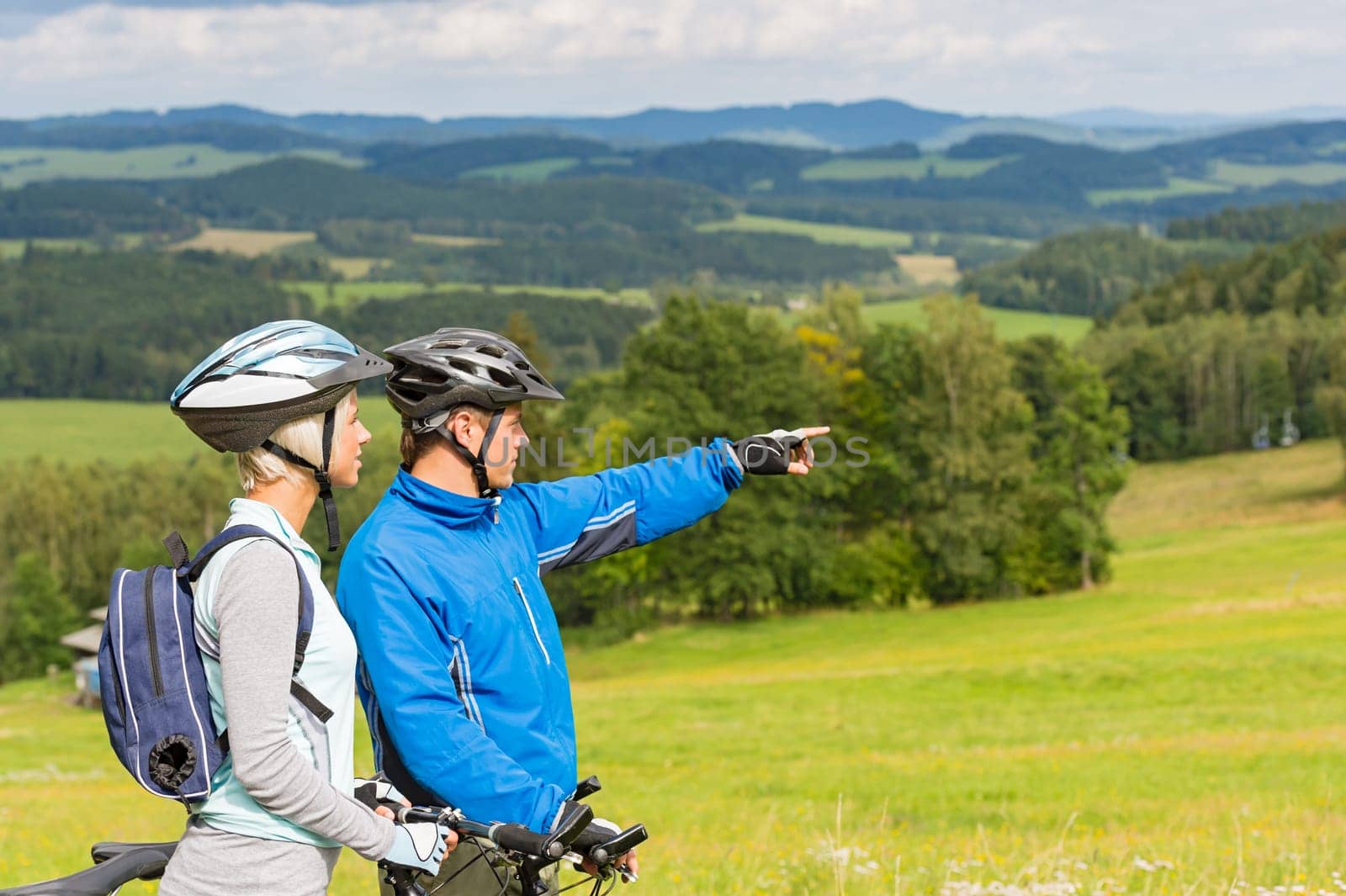 Sporty cyclist couple, man pointing to beautiful landscape