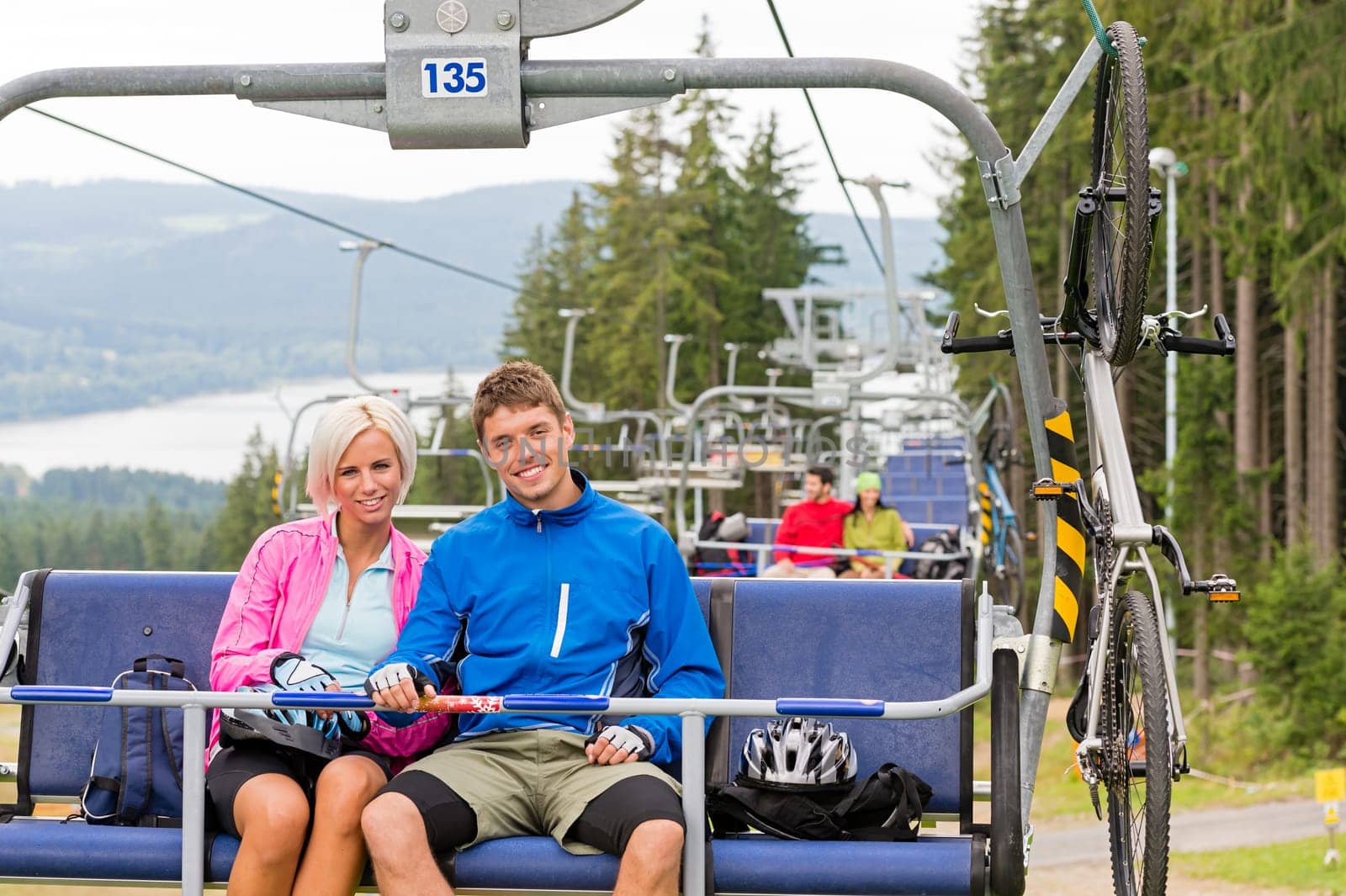 Chair lift going through forest while happy couple sitting