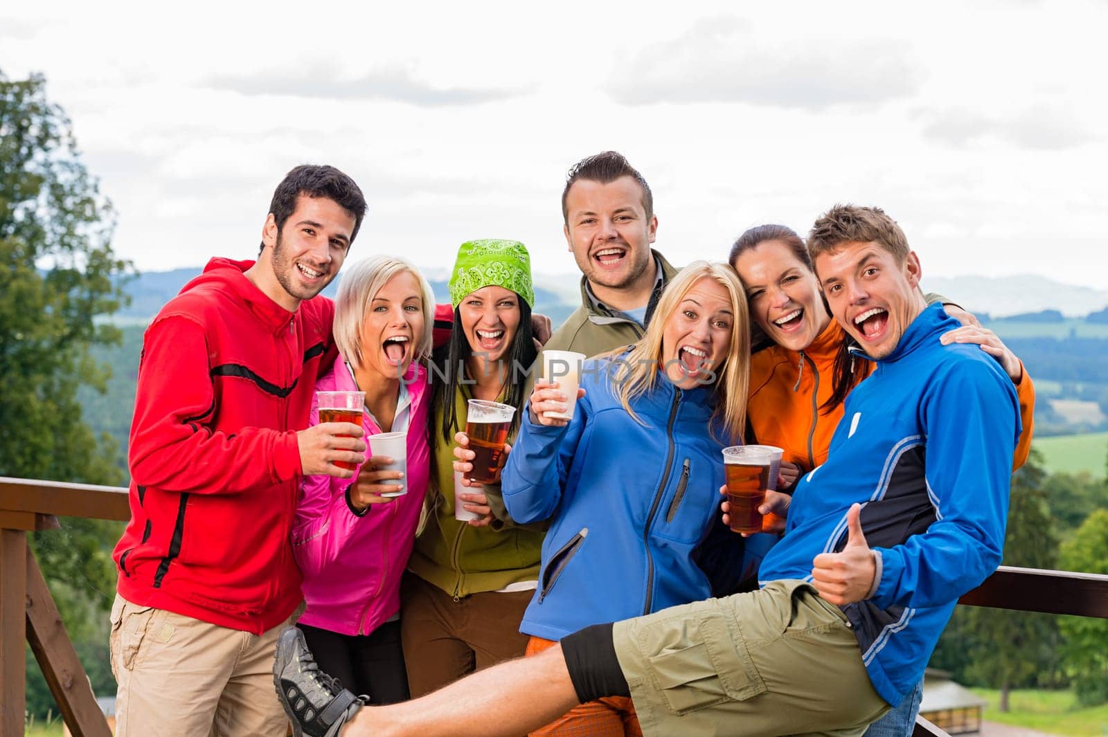 Smiling young people posing with beer and landscape background