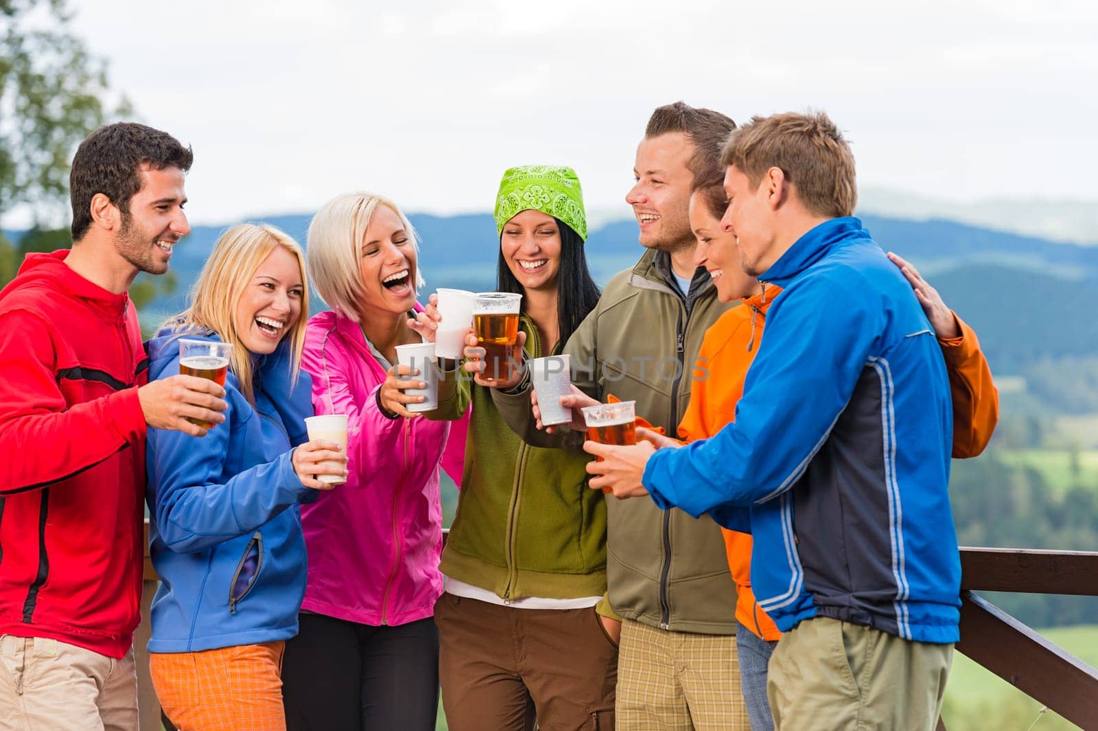 Happy young friends clinking glasses and drinking beer outdoors