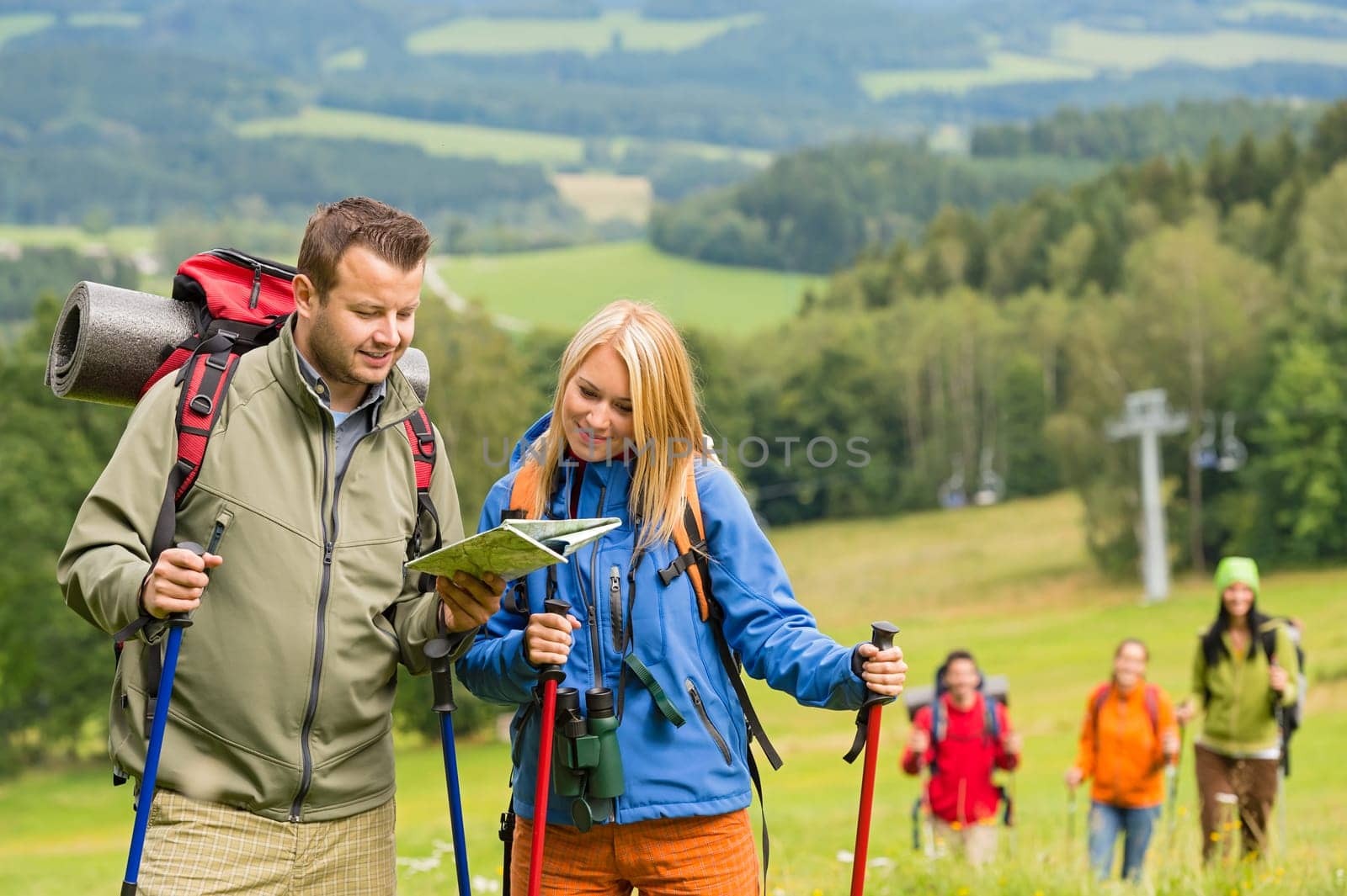 Young hiking couple with friends looking map to find track