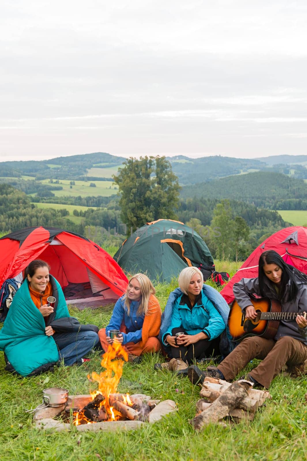Young girls camping with tents beside campfire in nature landscape