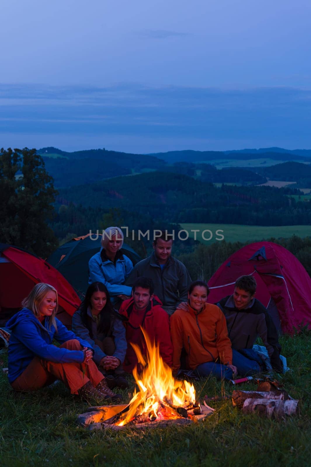 Friends watching fire together beside camp and tents in dark