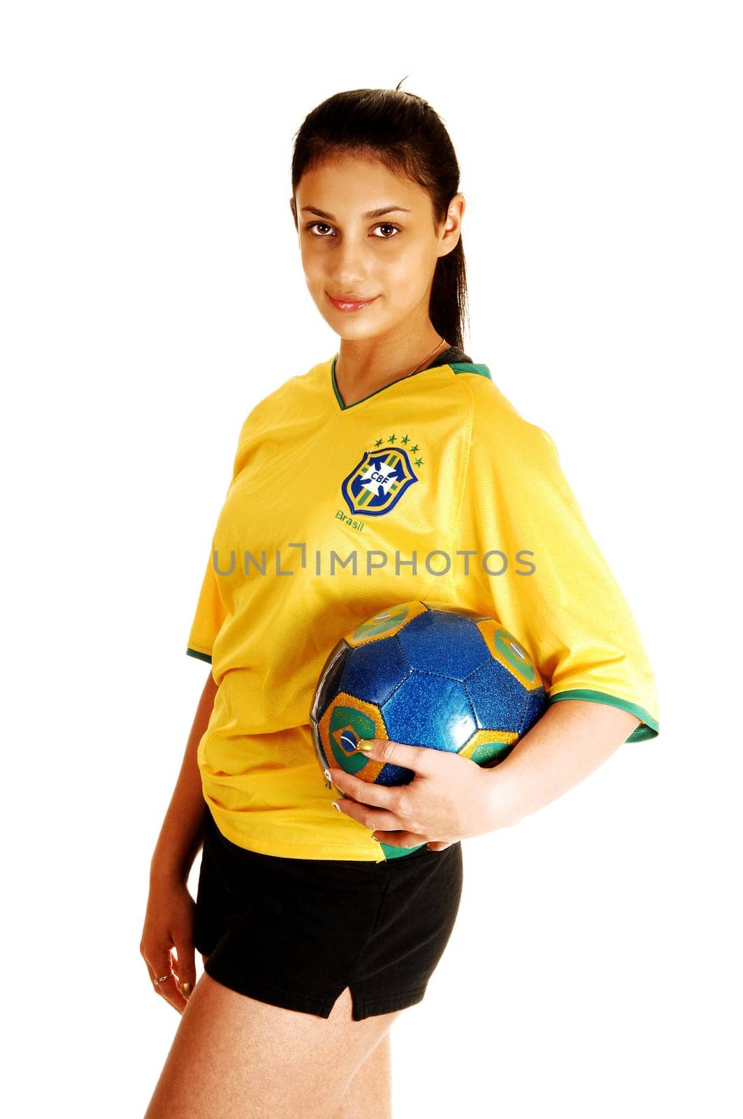 A young pretty soccer girl standing in her uniform, yellow top and black shorts, with a soccer ball in her hand for white background.