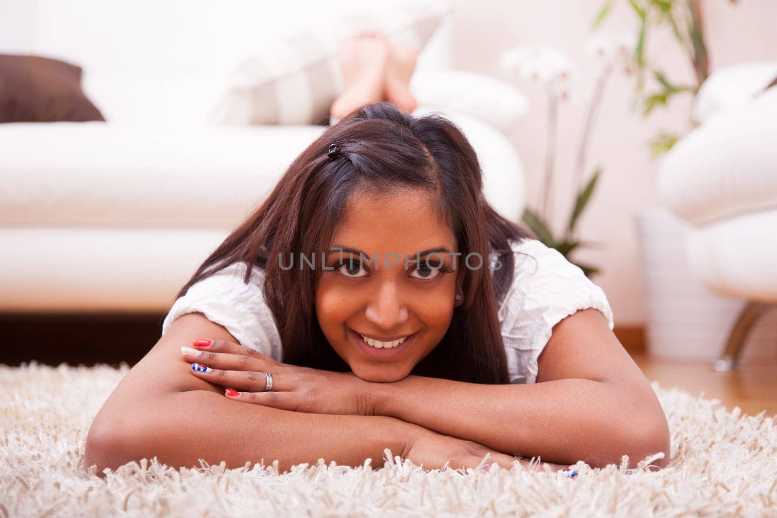 Young happy indian woman lying down on the floor in the living room