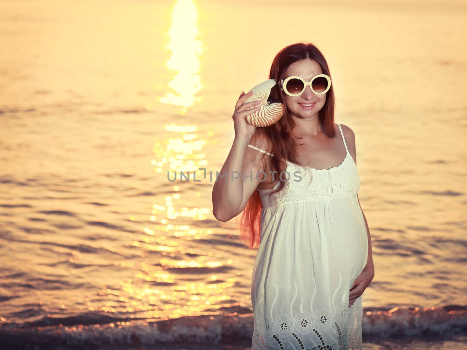 Beautiful pregnant woman at sunrise near the sea