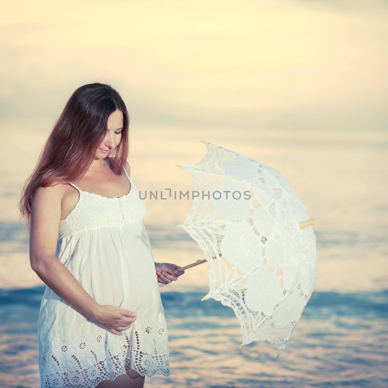 Beautiful pregnant woman at sunrise near the sea