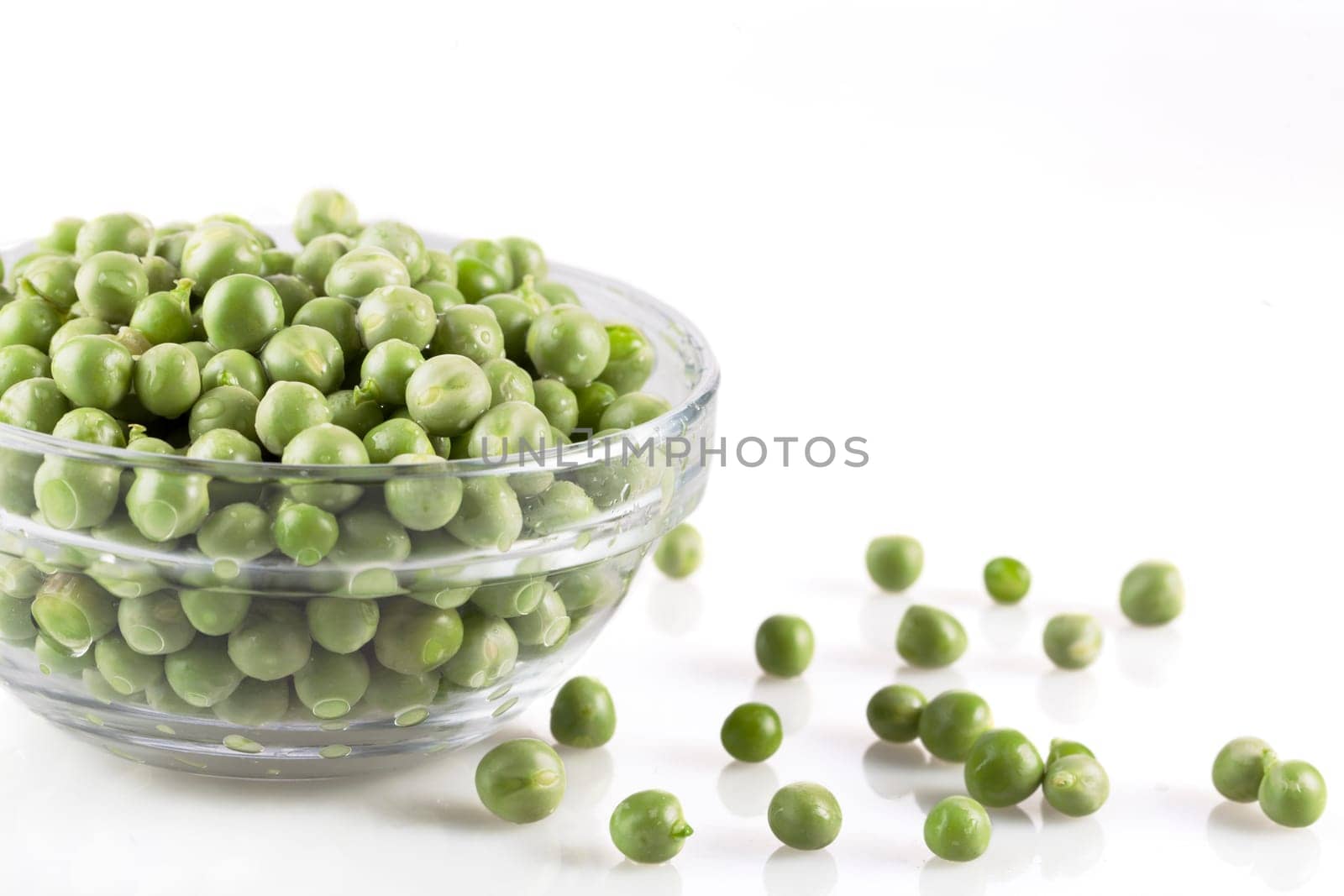 Fresh green peas in a glass bowl and on white surface.