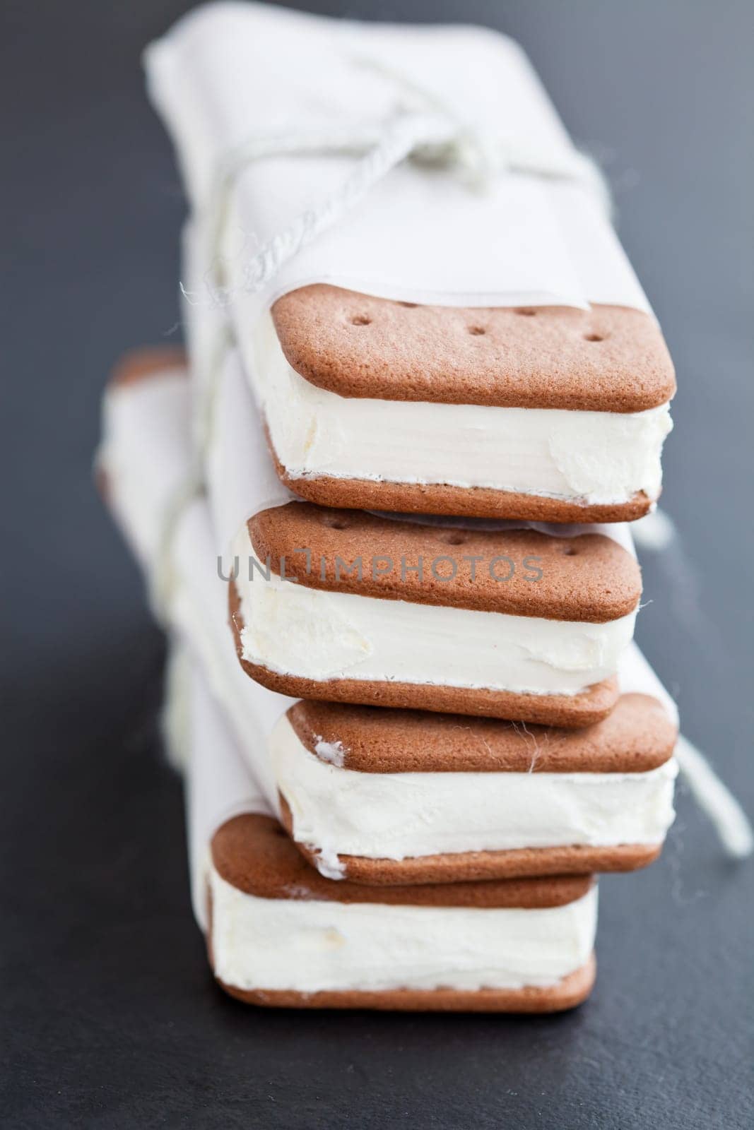 Closeup of stack of vanilla ice cream biscuits wrapped in white paper with string and bow on dark background