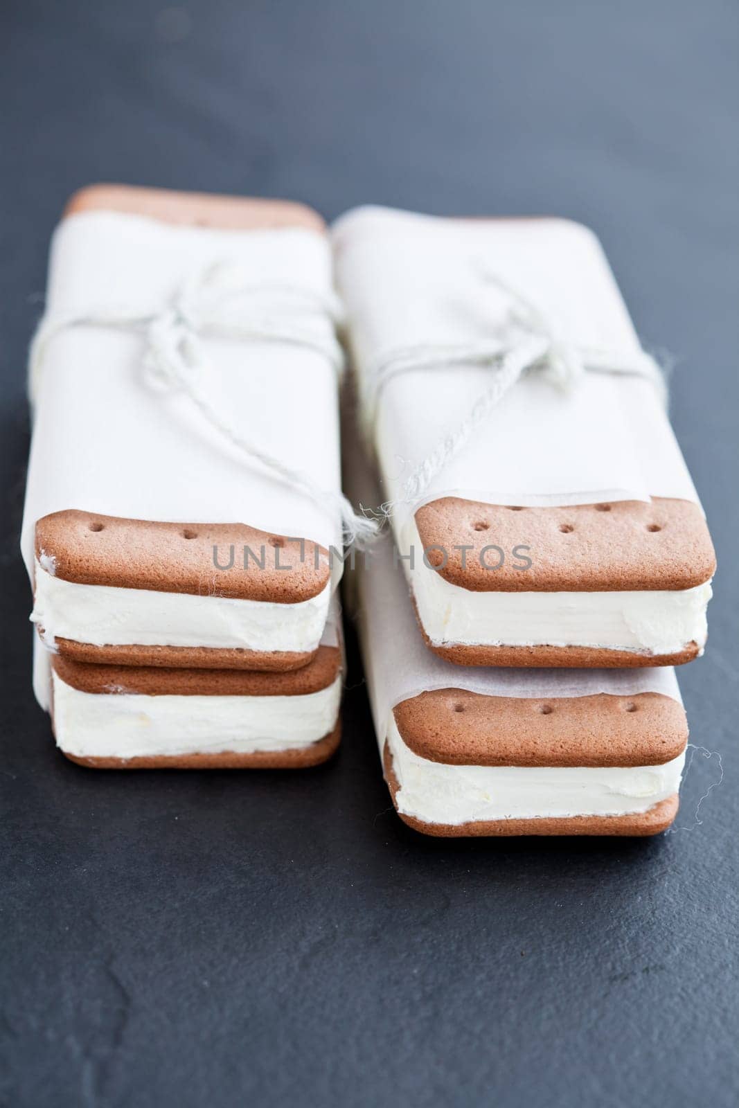 Closeup of two stacks of vanilla ice cream biscuits wrapped in white paper with string and bow on dark background