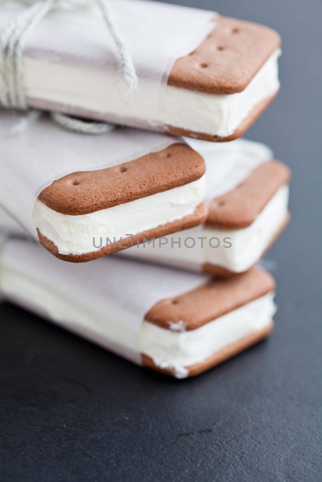 Closeup of stack of vanilla ice cream biscuits wrapped in white paper with string and bow on dark background