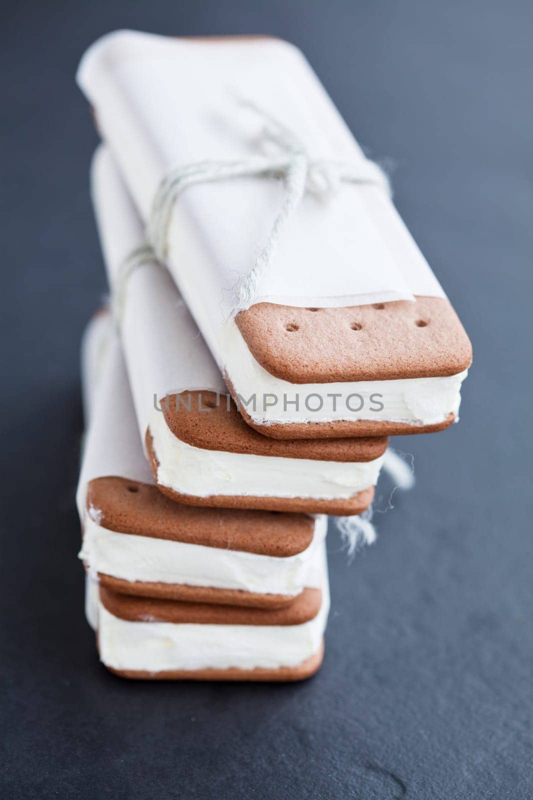 Closeup of stack of vanilla ice cream biscuits wrapped in white paper with string and bow on dark background