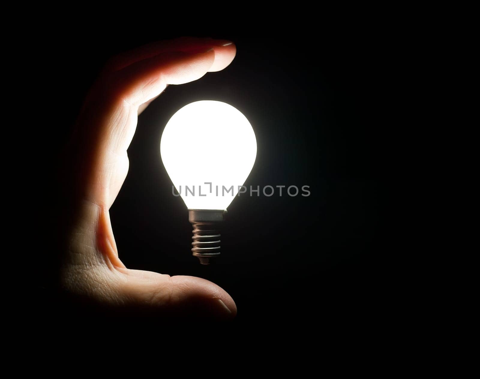 Hand grabbing floating light bulb on black background