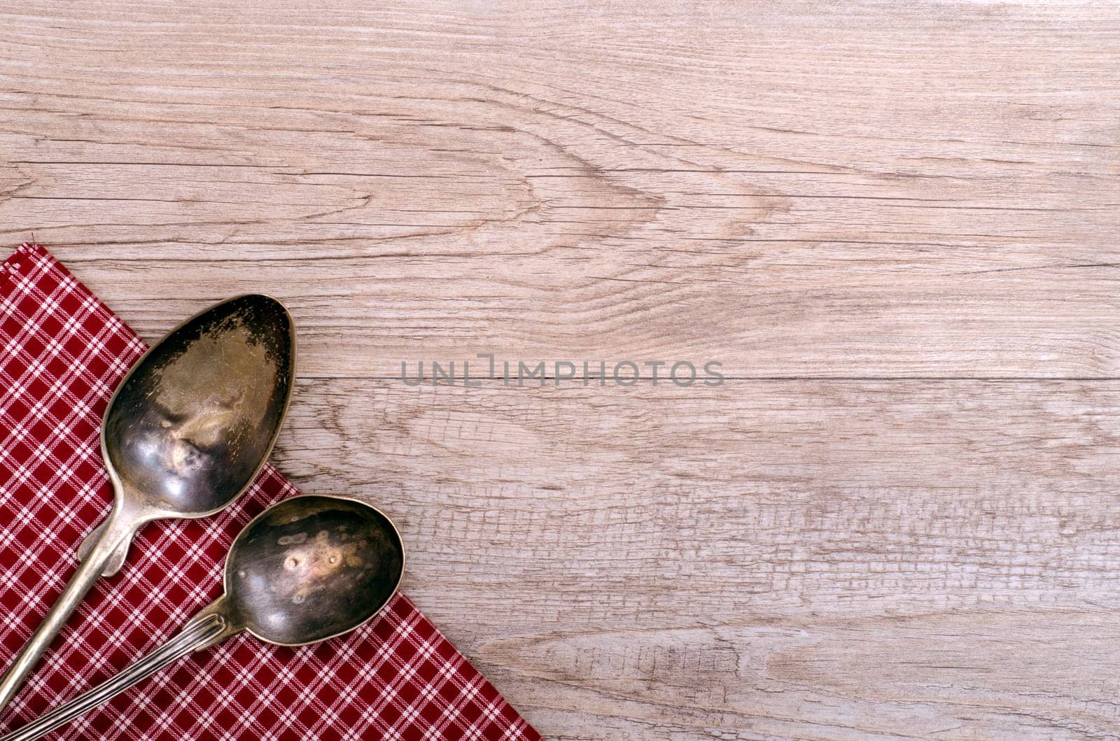 Two old silver spoons on checkered cloth and a weathered wood