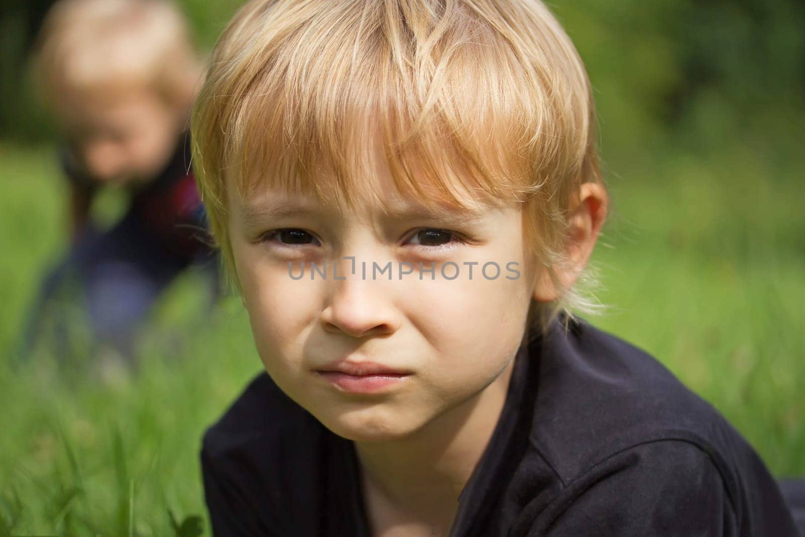 Portrait of a blond boy in the garden. His brother is in the background.