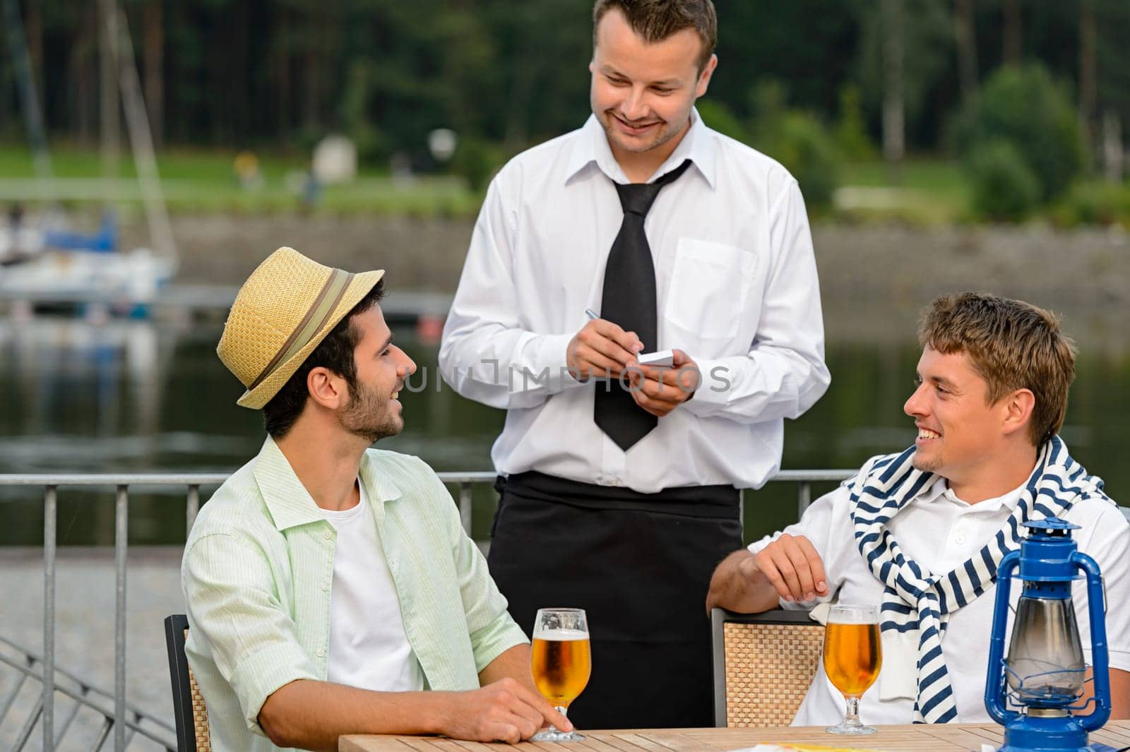 Smiling waiter taking order from men customers outdoor bar