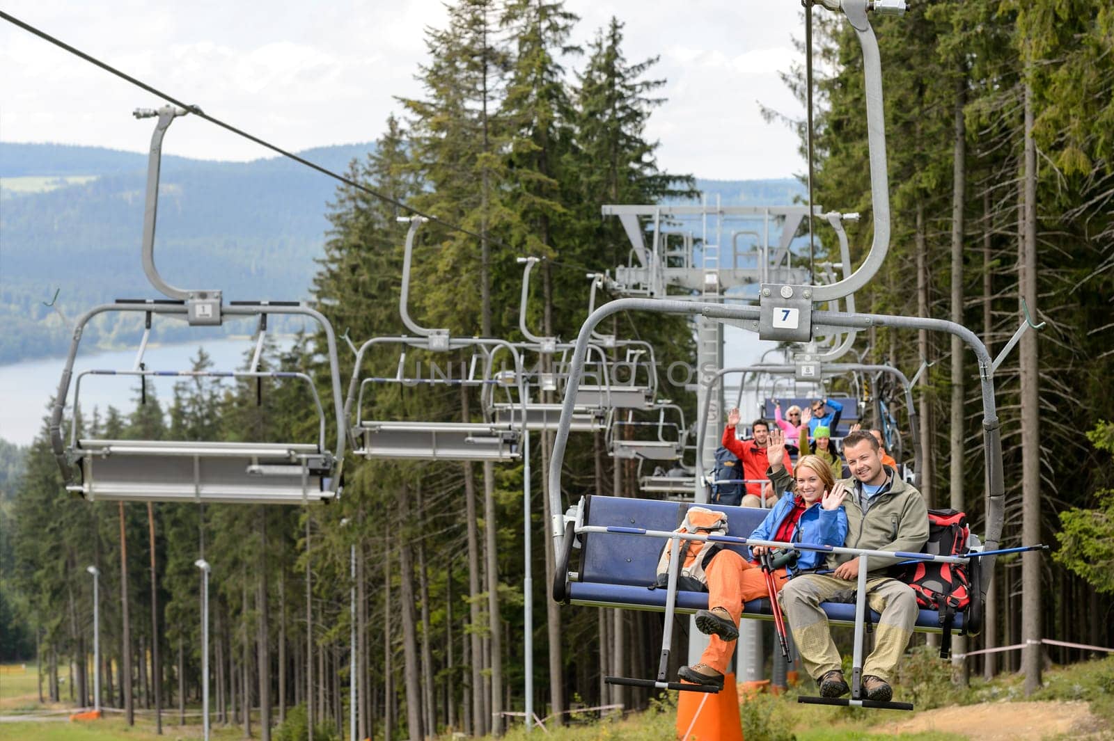 Waving young people sitting on chairlift going through forest