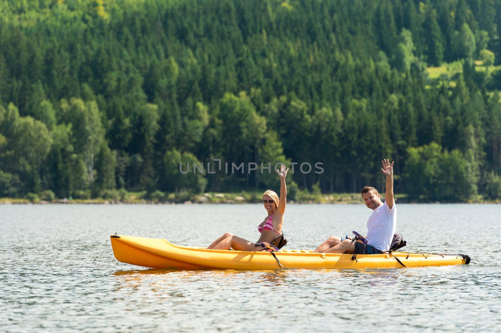 Young couple waving and rowing kayak on river summer vacation