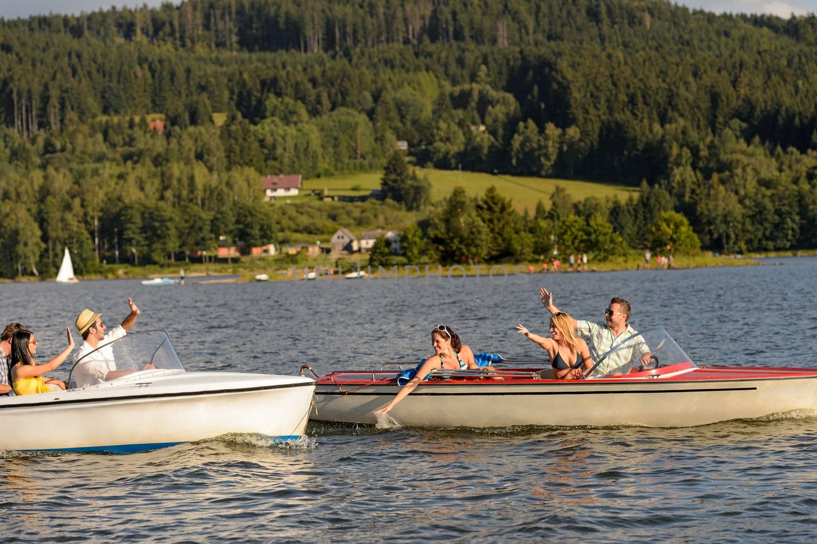 Young friends having fun in motorboats waving and splashing water