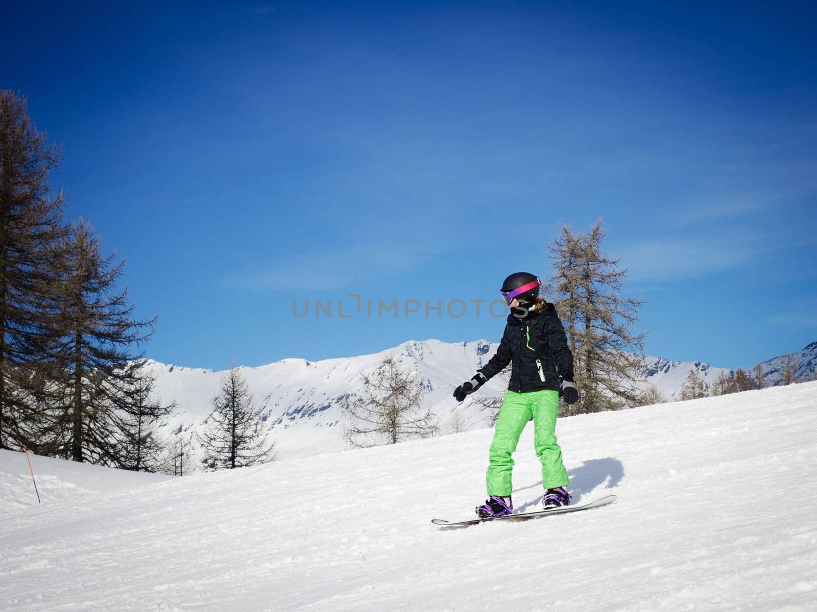 A girl or woman in green ski suit snowboarding in a sunny day
