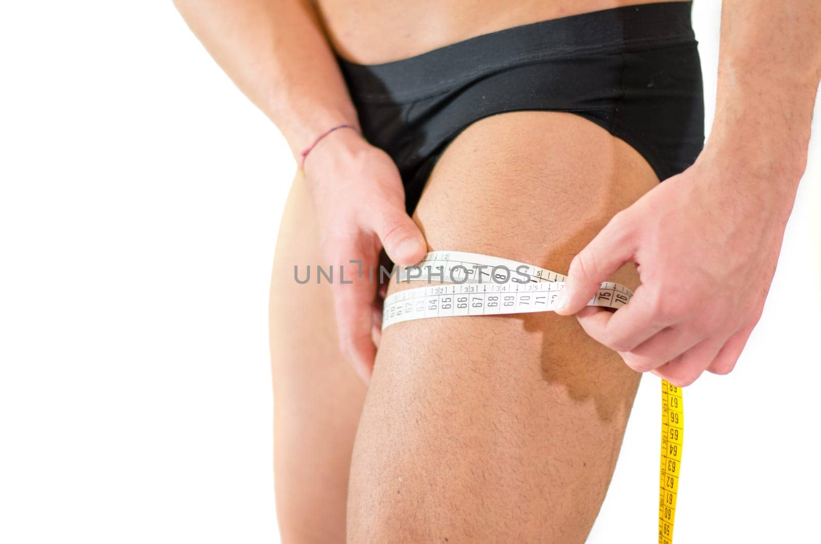 Close-up of young man measuring size of his thigh muscles with tape meter