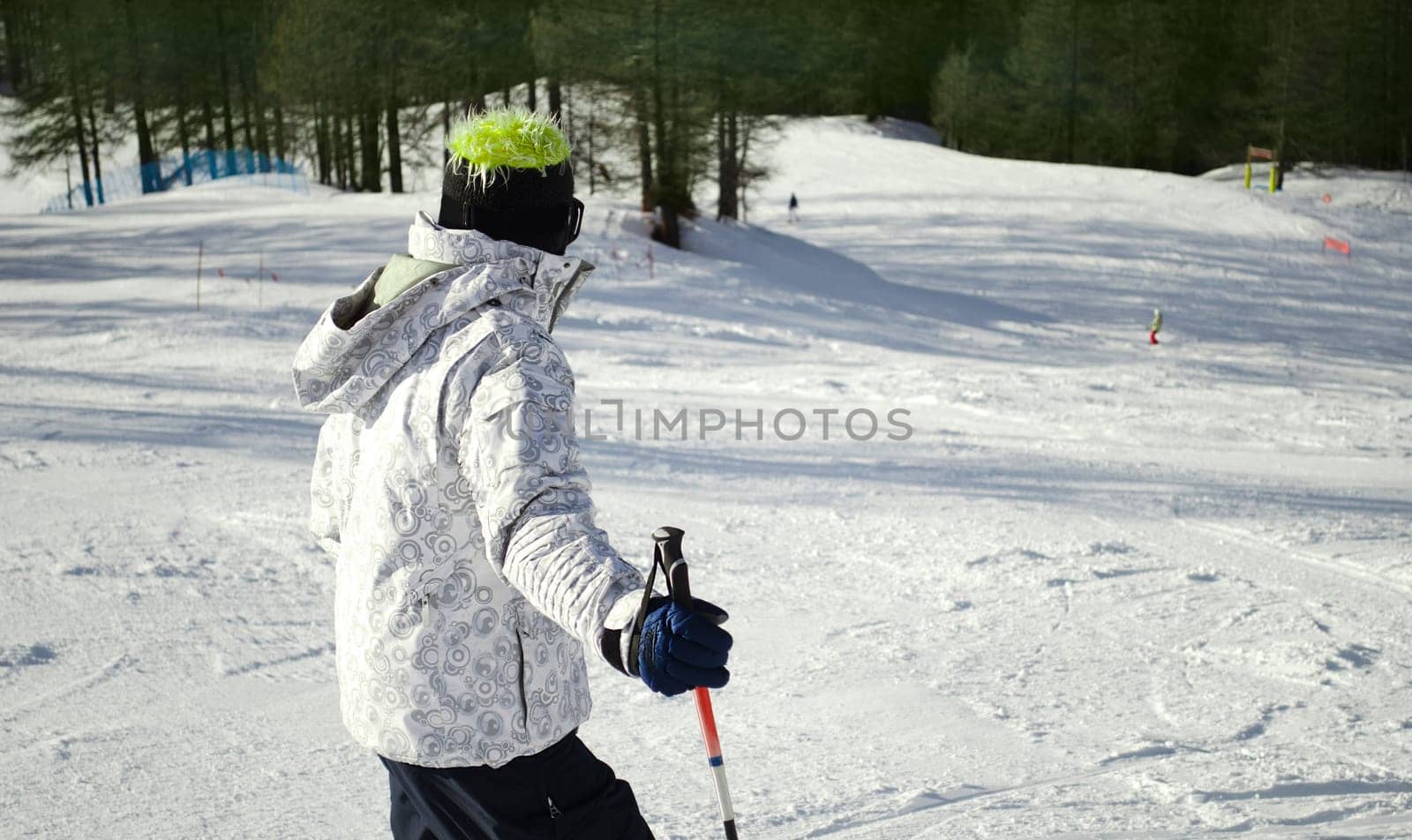 Skier or snowboarder seen from the back looking down the ski slope in sunny day