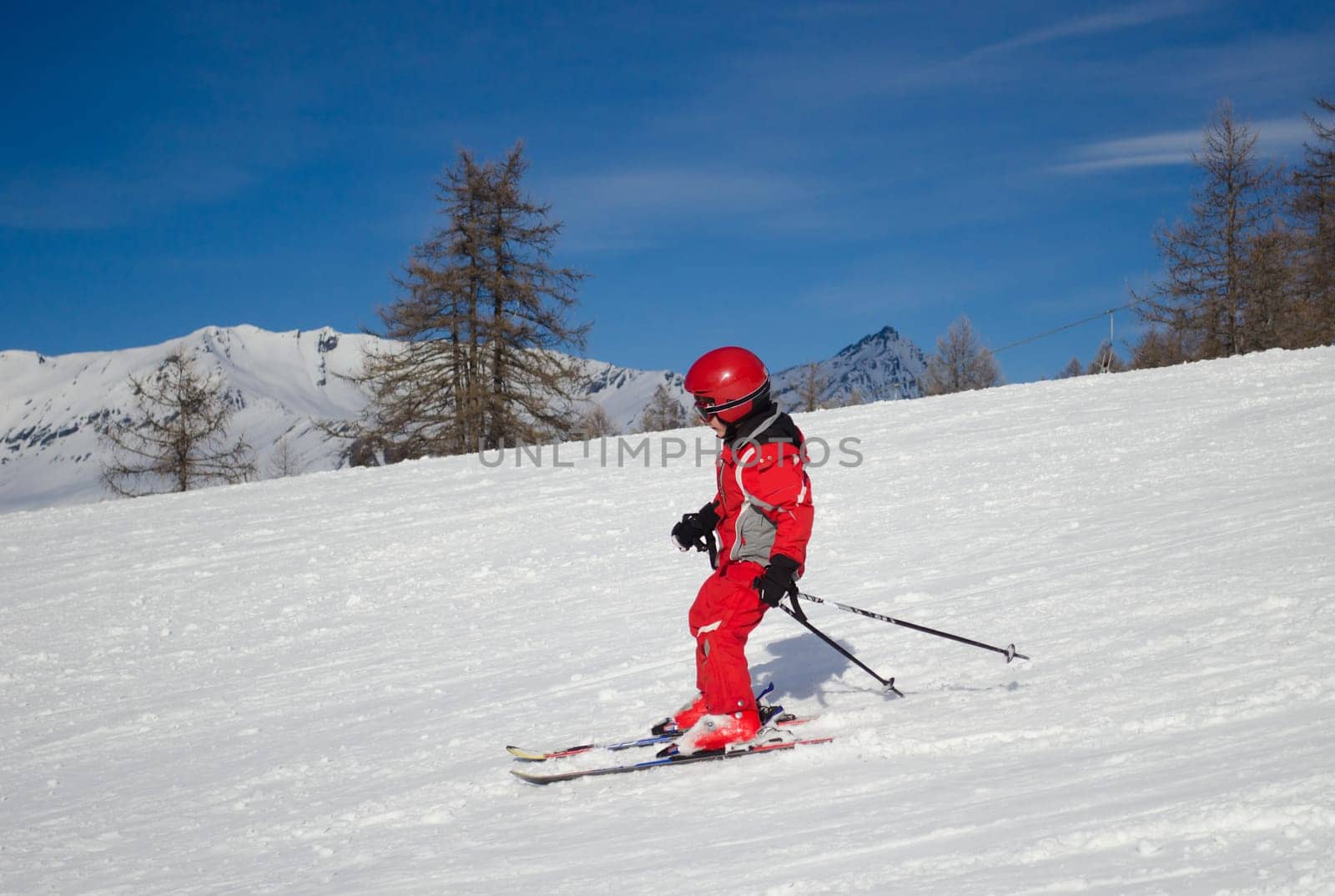 A kid in red ski suit skiing in a sunny day